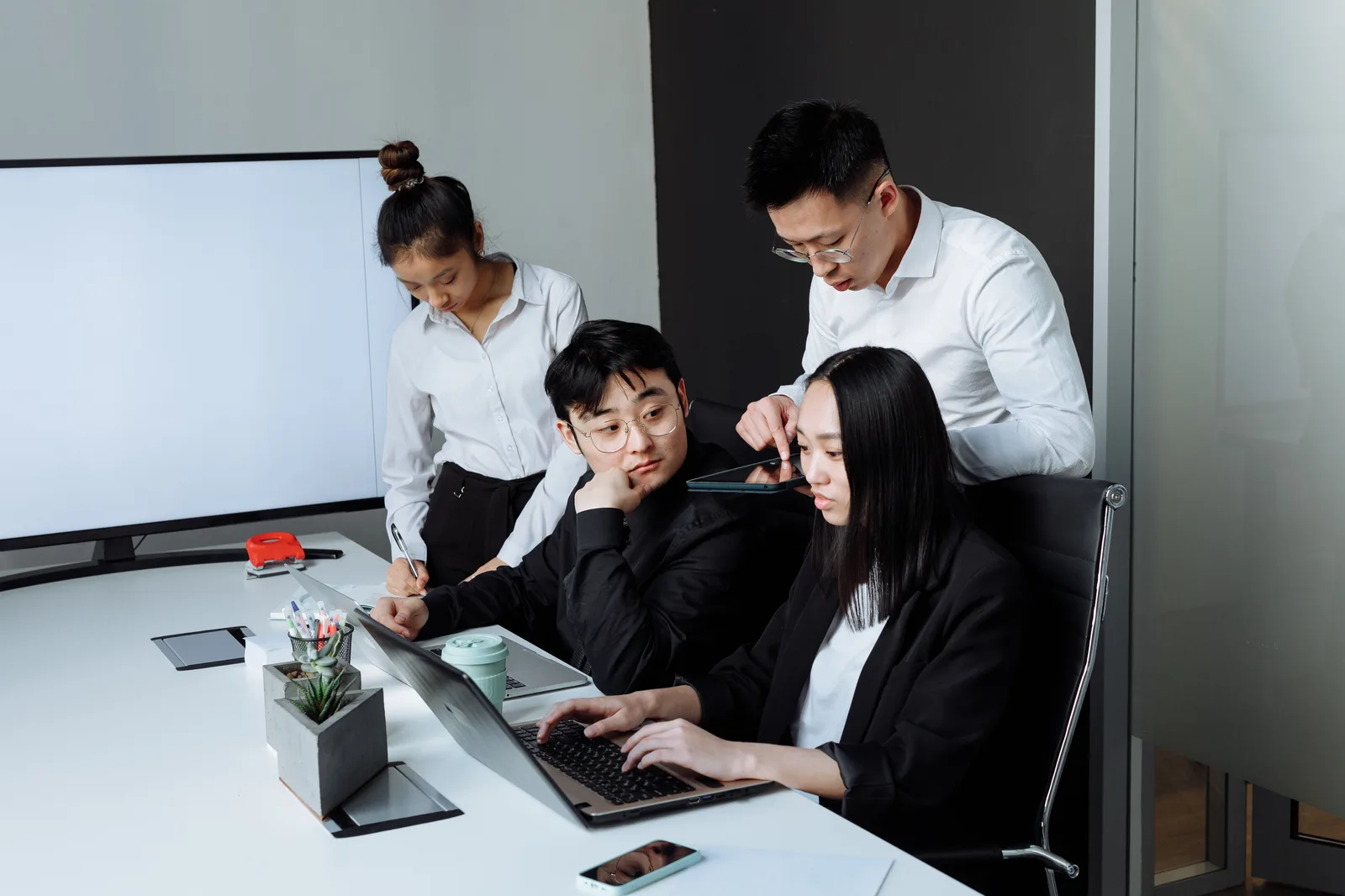Four professionals collaborating around laptops and a tablet in a modern office